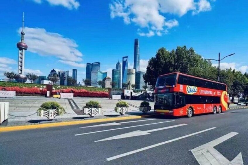 A red double-decker bus on a city street with modern skyscrapers and a tower in the background. 2