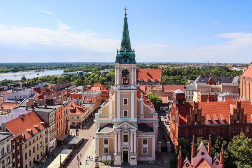 A historic church with a tall spire, surrounded by red-roofed buildings and a river in the background. 1
