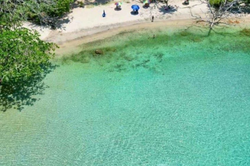 A beach with clear turquoise water, a sandy shore, and some umbrellas. 1