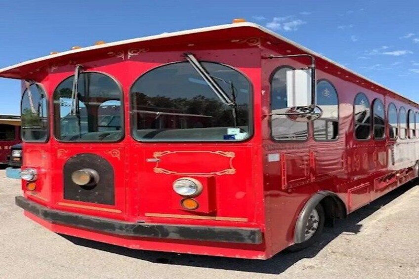 A red bus with large windows and a front grill, parked on a concrete surface. 3