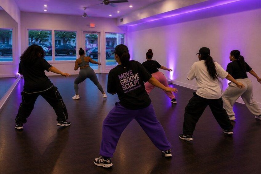 A dance class in a studio with large windows and purple lighting. 1