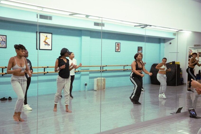 A dance class in a studio with a mirror wall, ballet barres, and a few pictures on the wall. 3