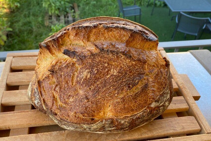 A loaf of artisan bread on a wooden table outdoors. 2