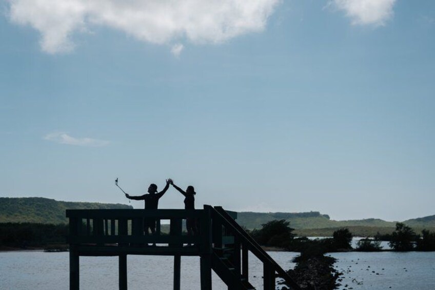 A wooden structure over water with two people on it, one holding a stick. 3