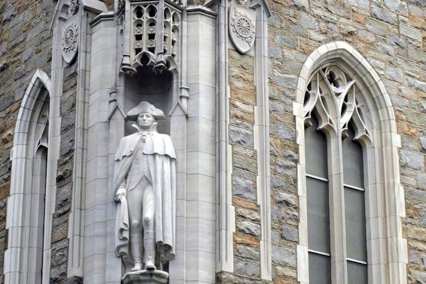 A stone building with a statue of a man in period clothing, arched windows, and decorative stonework. 4