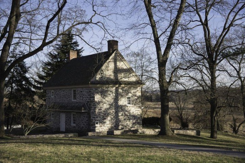 A stone house with a gabled roof, surrounded by trees and a grassy yard. 5