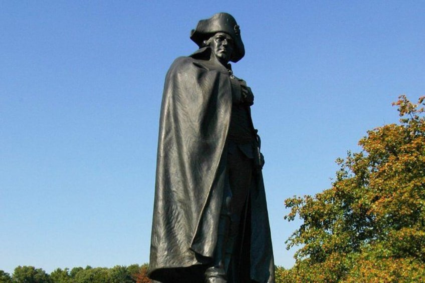 A statue of a person in a long robe, standing outdoors with trees in the background. 2
