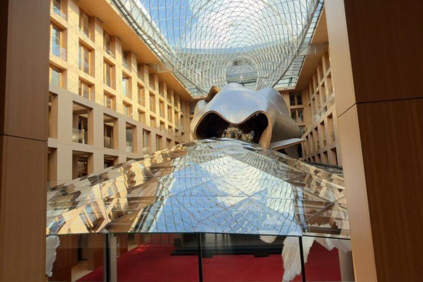 A modern building with a glass ceiling, a unique metallic sculpture, and a red carpet. 3