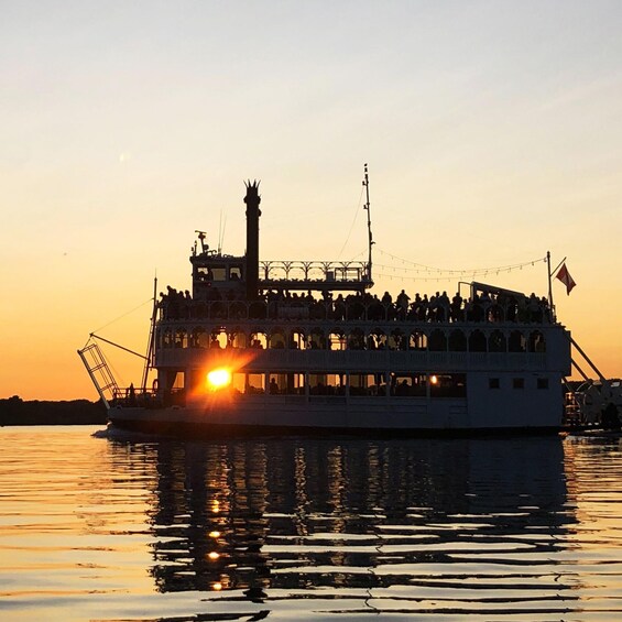 Ein Flussdampfer mit belaubten Passanten vor einem Sonnenuntergang. 1