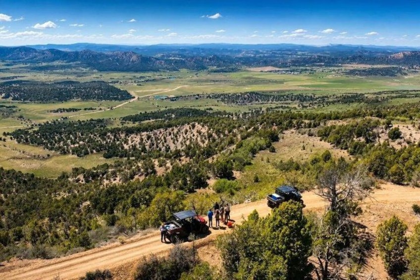 A mountainous landscape with a dirt road, a vehicle, and a group of people. 1