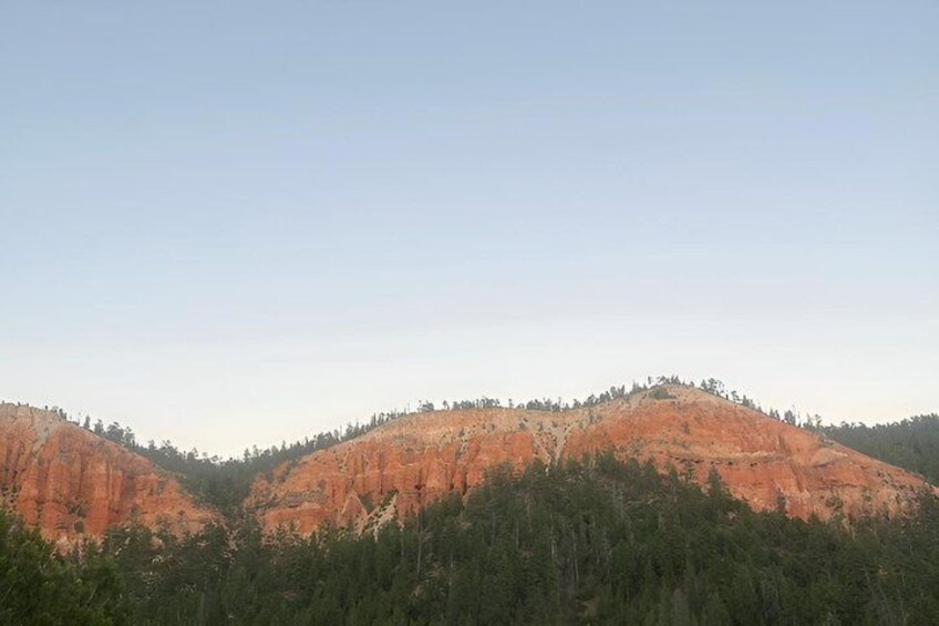 A landscape with two prominent red hills, dense green forest at the base, and a clear sky. 5