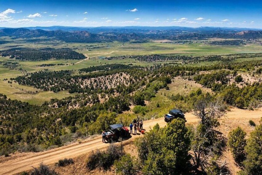 A mountainous landscape with a dirt road, a vehicle, and a small group of people. 2