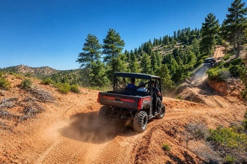 A red off-road vehicle on a dirt trail surrounded by trees and hills. 4