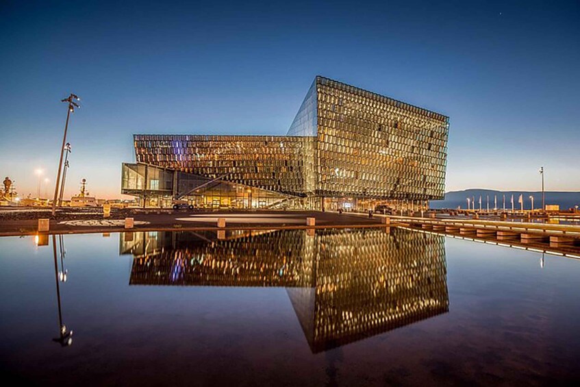 A modern glass building with a unique angular design, reflecting on a calm body of water. 2