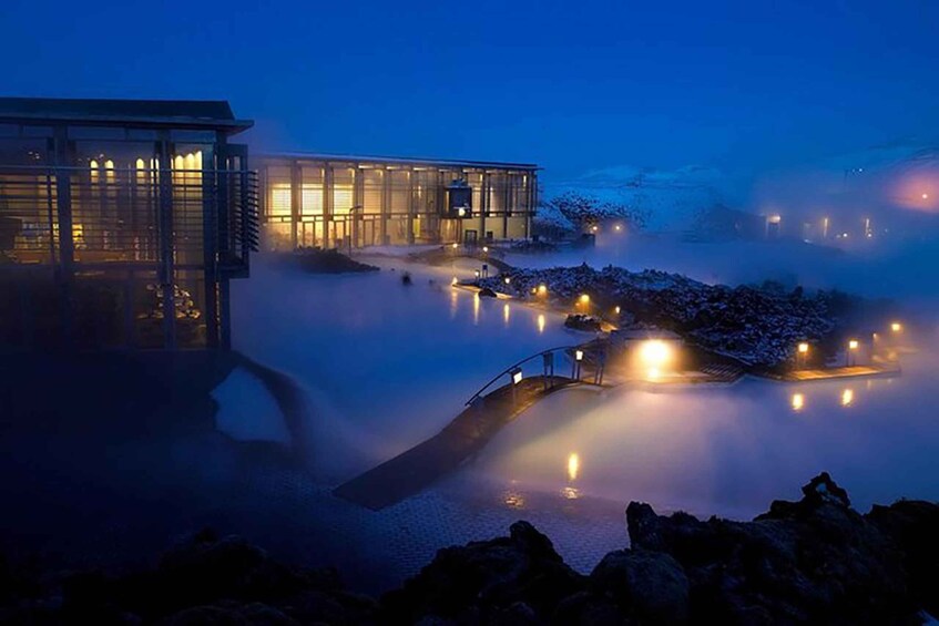 A modern building with glass windows and a pool area with mist and lights. 1