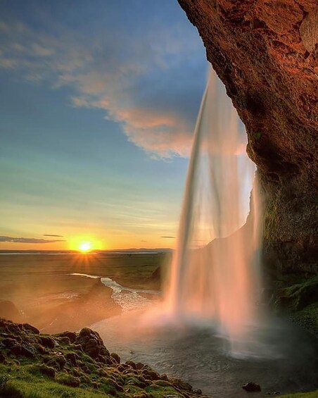 A waterfall cascading into a body of water, a rocky cliff, and a sunset in the background. 4