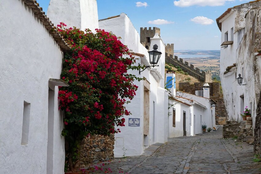 A narrow cobblestone street flanked by white buildings with a stone wall and a sign reading 'RUA DE SANTIAGO'. 5