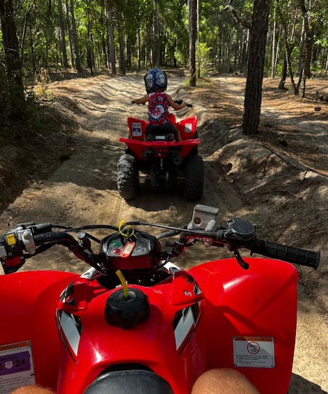 A red ATV with a child riding it on a dirt trail in a forest. 5