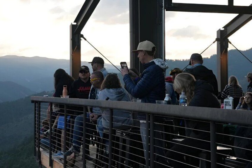 A group of people seated on a balcony overlooking a mountainous landscape. 2