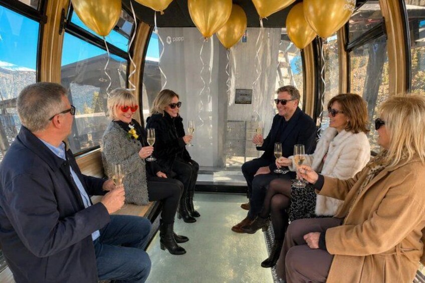 A group of people sitting on a bench inside a building with large windows, holding champagne glasses. 5
