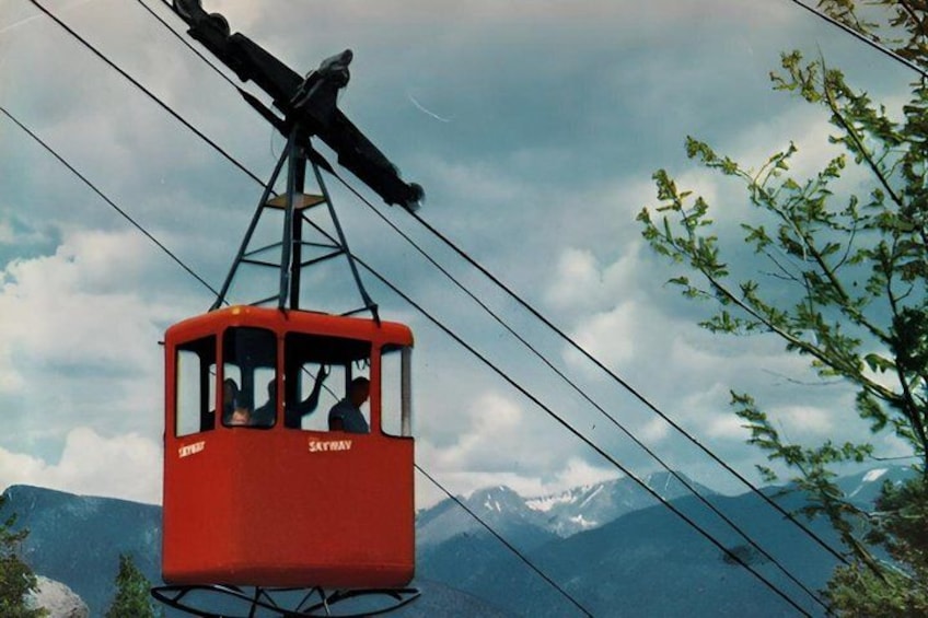 A red cable car suspended by cables against a backdrop of mountains and a cloudy sky. 2