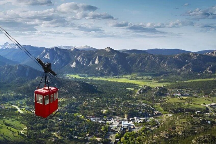 A red cable car suspended over a mountainous landscape with a town below. 1