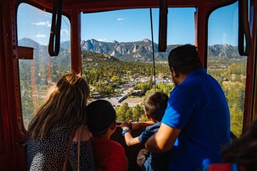 A family inside a cable car overlooking a mountainous landscape with a river and buildings. 4