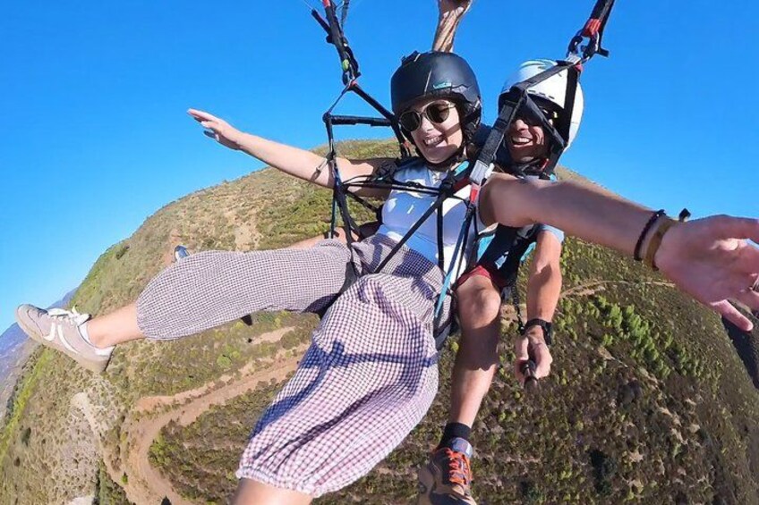 Two people skydiving with parachutes, one wearing a checkered dress and the other in a sleeveless top, over a mountainous landscape. 1