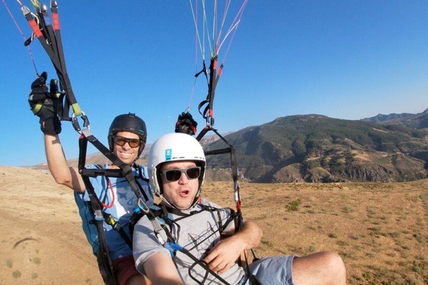 Two people paragliding with a mountainous landscape in the background. 3