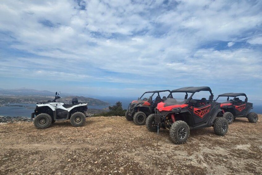 Four off-road vehicles parked on a dirt surface with a scenic view of a coastline and mountains in the background. 3