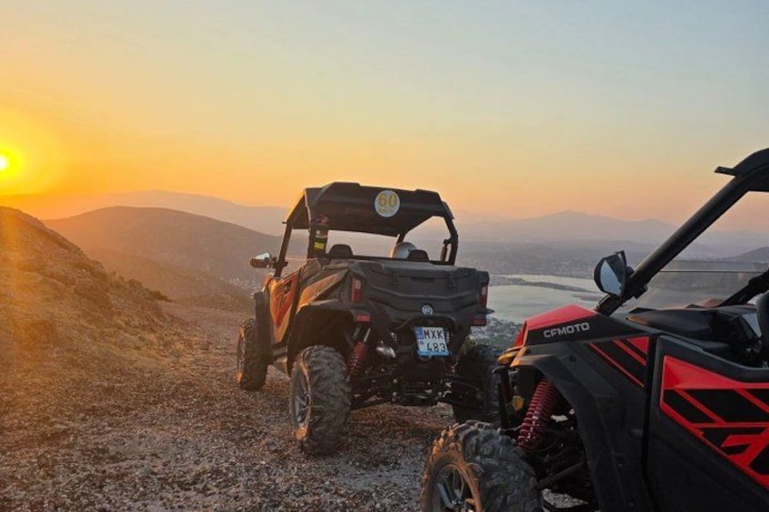 Two off-road vehicles parked on a rocky terrain with a sunset in the background. 1