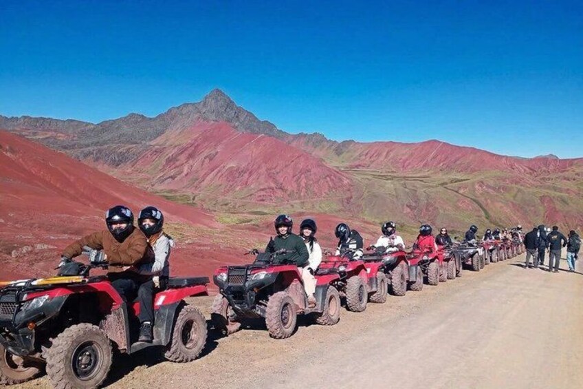 A group of people on ATVs lined up on a dirt road with a mountainous landscape in the background. 1