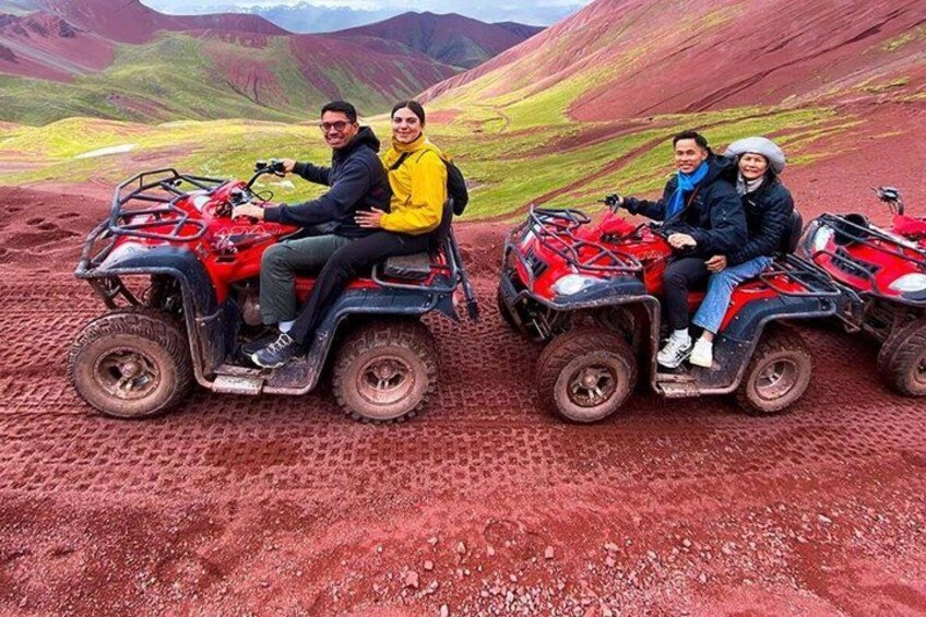 Three people on red ATVs in a rugged, red-hued landscape with hills in the background. 5