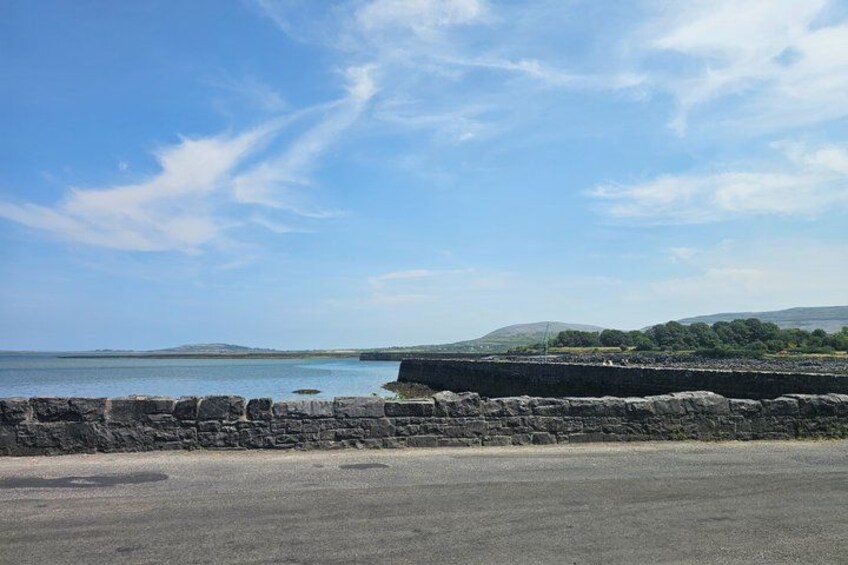 A coastal landscape with a stone wall, a clear sky, and distant hills. 2