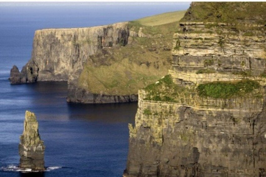 A coastal cliff with layered rock formations and a prominent rock pillar. 1