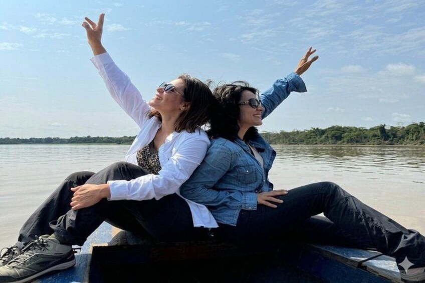Two people sitting on a boat with their arms raised, facing a calm body of water and a clear sky. 4