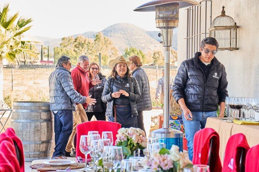 A group of people gathered around a table with wine glasses, outdoors with mountains in the background. 4
