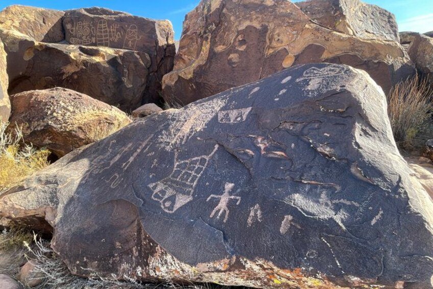 A large rock with petroglyphs including a human figure and geometric shapes. 5