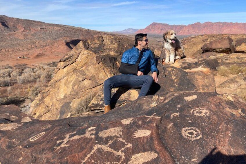 A person sitting on a rock with a dog nearby in a desert landscape. 1