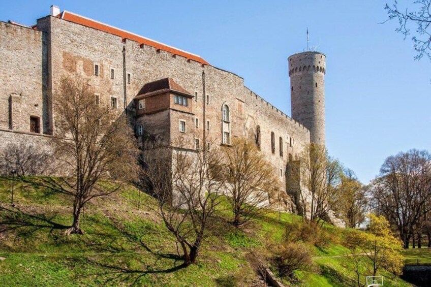 A historic stone building with a tower, surrounded by trees and grassy terrain. 3