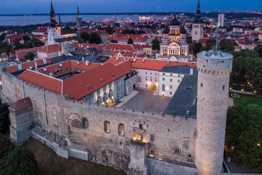 A historic castle with a red roof, a prominent tower, and a domed building in the background. 2