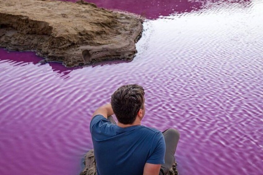 A person sitting on a rock by a body of water with purple water. 1