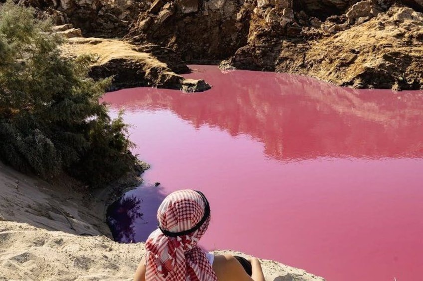 A person overlooking a red body of water surrounded by rocky terrain and sparse vegetation. 3