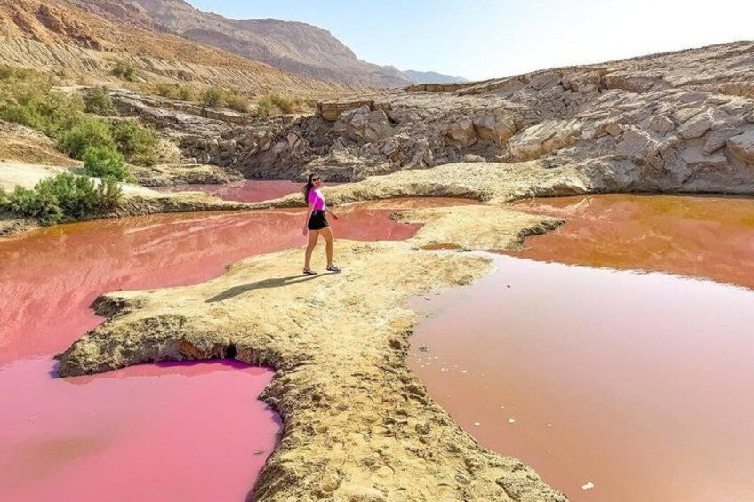 A person standing on a rocky outcrop with red mineral pools. 5