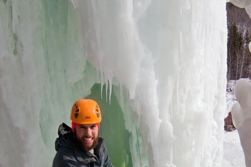 A person wearing an orange helmet standing in front of a large ice formation. 5