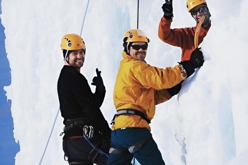 Three people in yellow helmets and winter gear climbing a snowy slope. 4