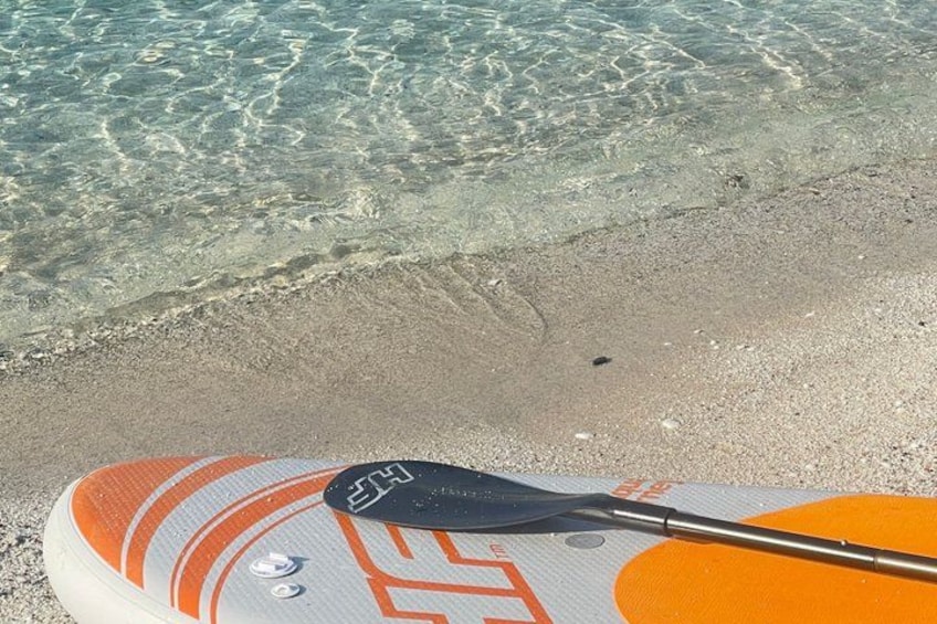 A paddle resting on a kayak on a sandy beach with clear water. 4