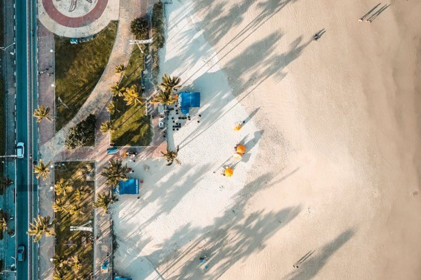 An aerial view of a beach with palm trees, a road, and a few people. 5