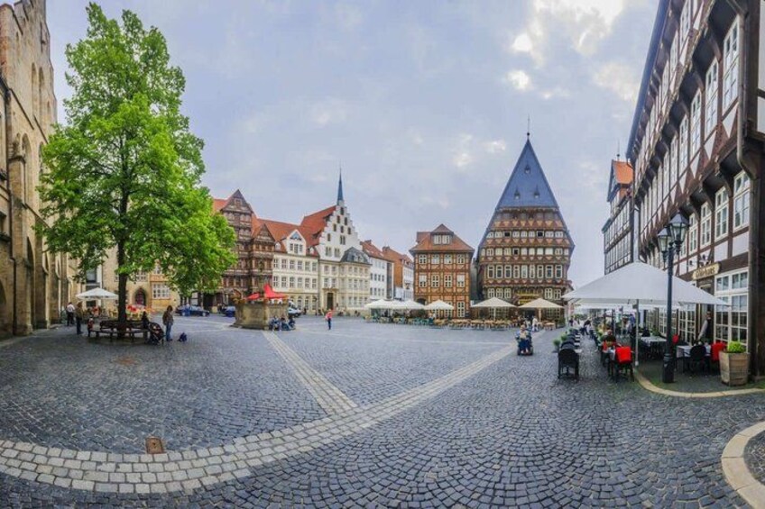 A cobblestone square with historic buildings, a prominent church spire, and outdoor seating areas. 3