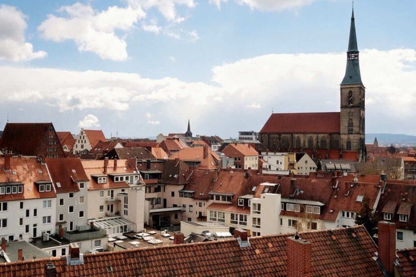 A town with red-roofed buildings, a prominent church with a tall spire, and a clear blue sky. 1